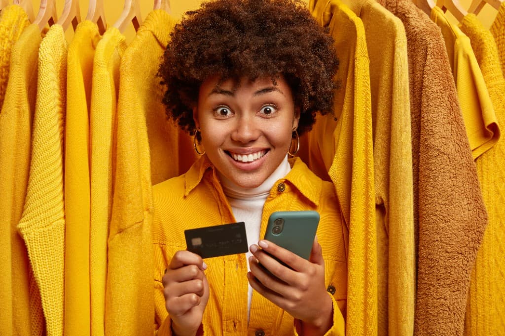 Cliente souriante tenant une carte bancaire et un smartphone pour payer en ligne